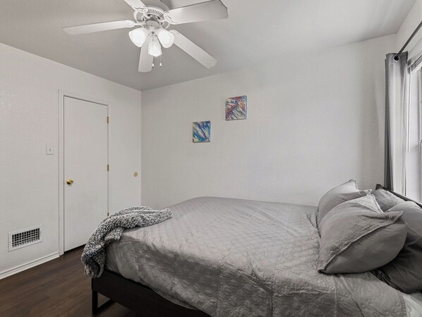 Ein Schlafzimmer mit einem Bett, einem Deckenventilator, einer Tür und zwei an der Wand befestigten Bildern.