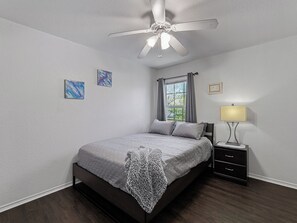 Ein Schlafzimmer mit einem Bett, einem Nachttisch, einer Lampe, einem Deckenventilator und zwei Bildern an der Wand.