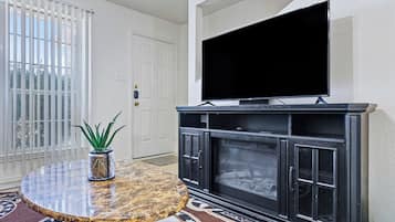 A living room with a flat-screen TV mounted above a black entertainment center, a round marble table with a potted plant, and a patterned rug.
