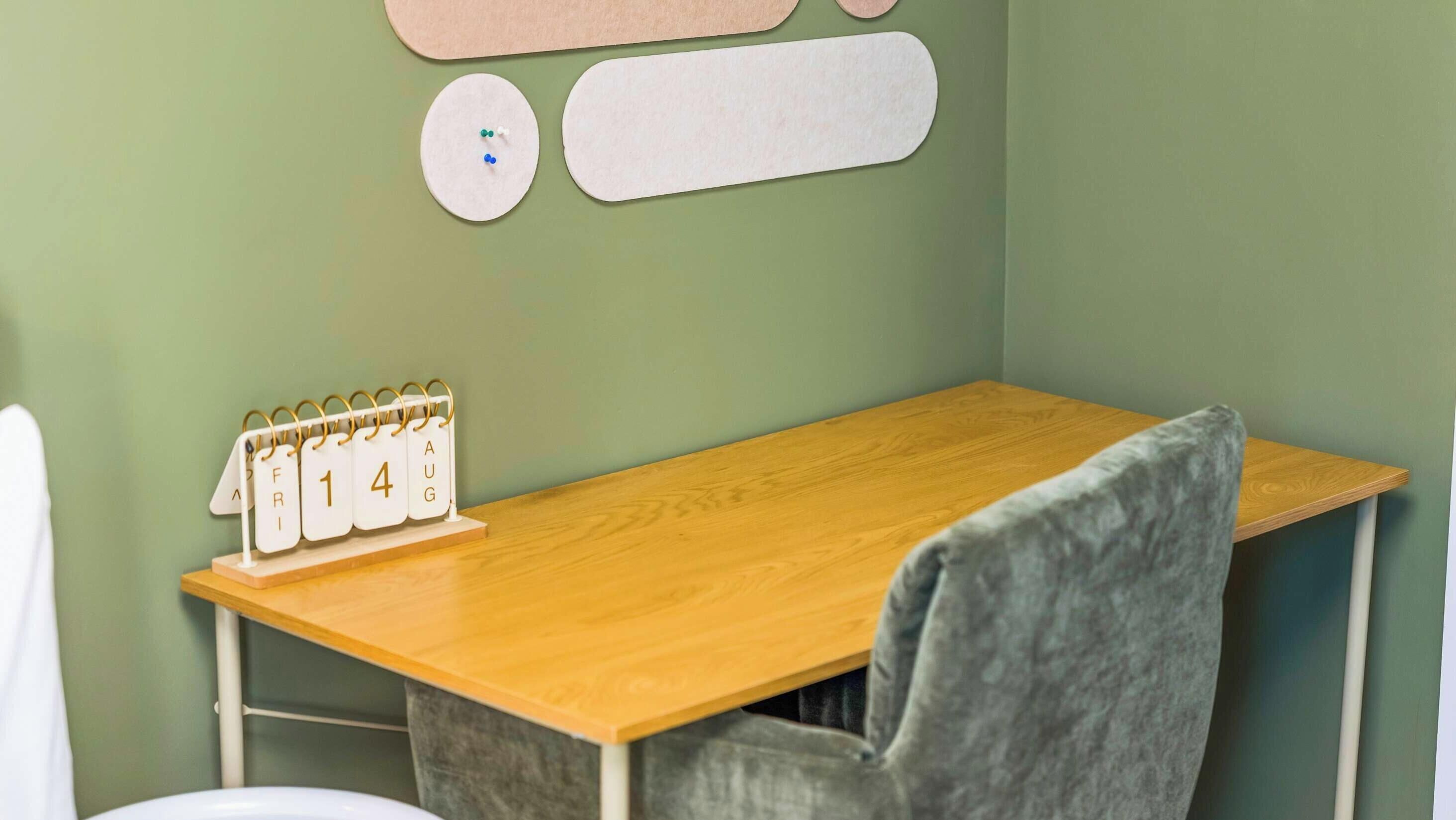 A small room with a wooden desk, a chair, a calendar, and a wall-mounted shelf.