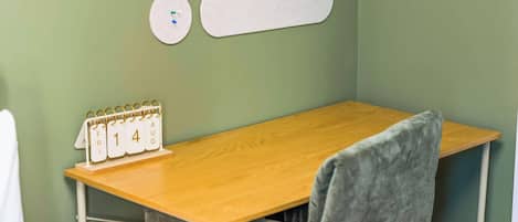 A small room with a wooden desk, a chair, a calendar, and a wall-mounted shelf.