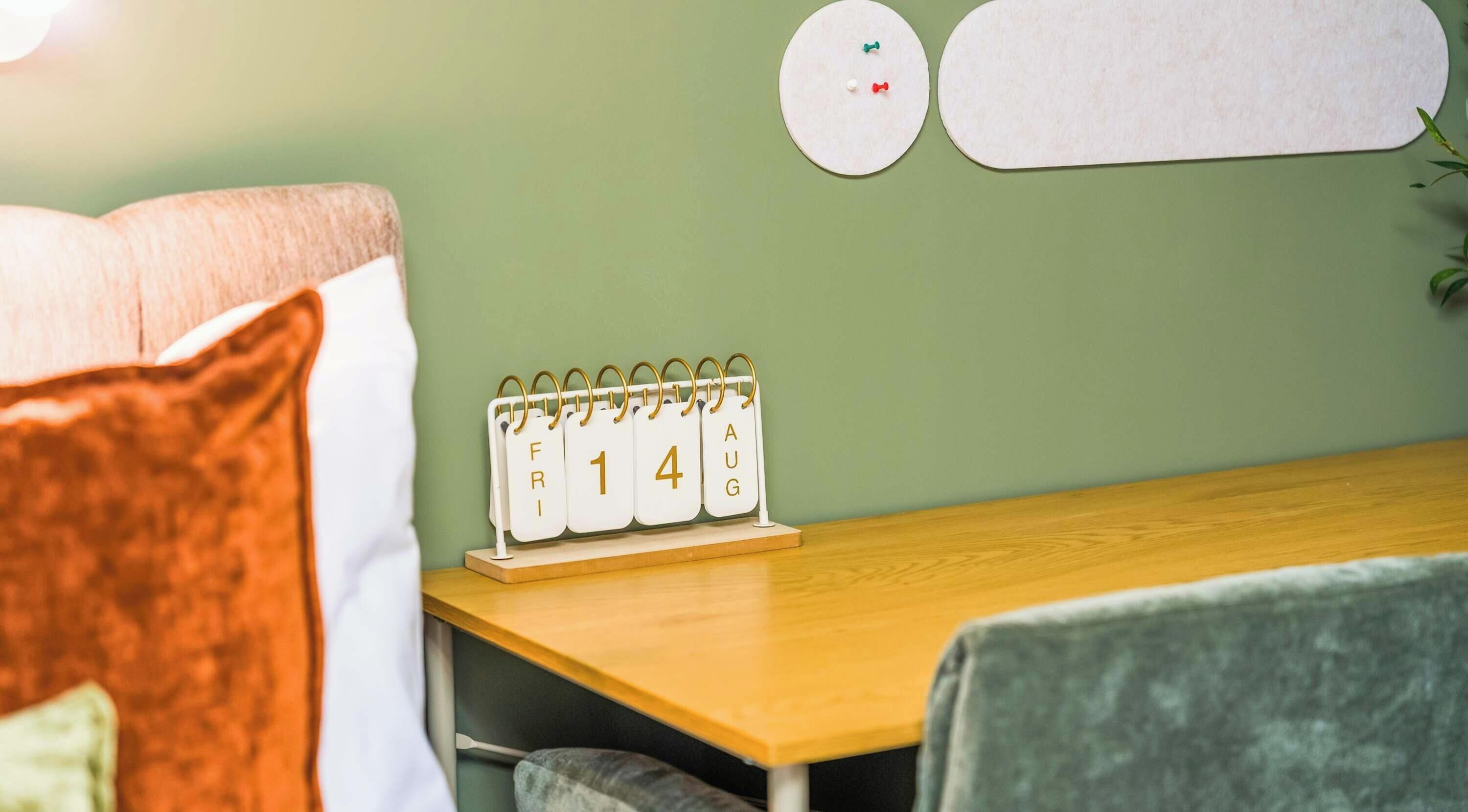 A room with a wooden table, a calendar, and a green wall.