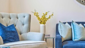 Un salon comprenant un fauteuil à capitons, une table d’appoint ornée d’un vase de fleurs jaunes et un canapé bleu avec des coussins assortis.