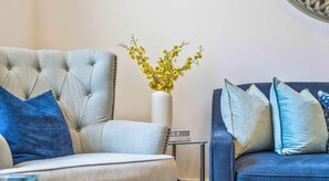 A living room with a tufted armchair, a side table with a vase of yellow flowers, and a blue sofa with matching cushions. - Central London Apartment with Free WiFi by Rapid Returns (London)
