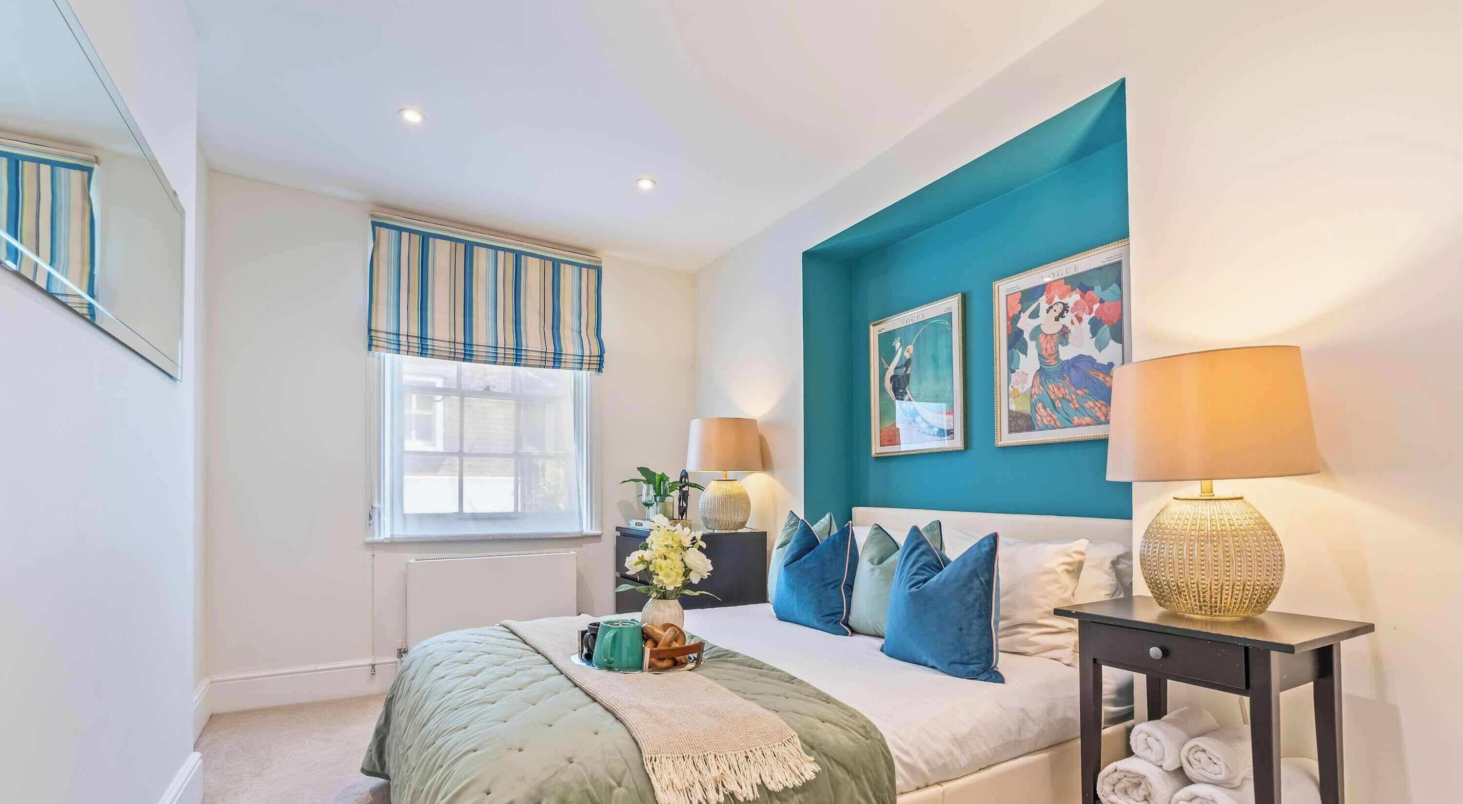 A bedroom with a bed, bedside tables, a window with curtains, and wall art.