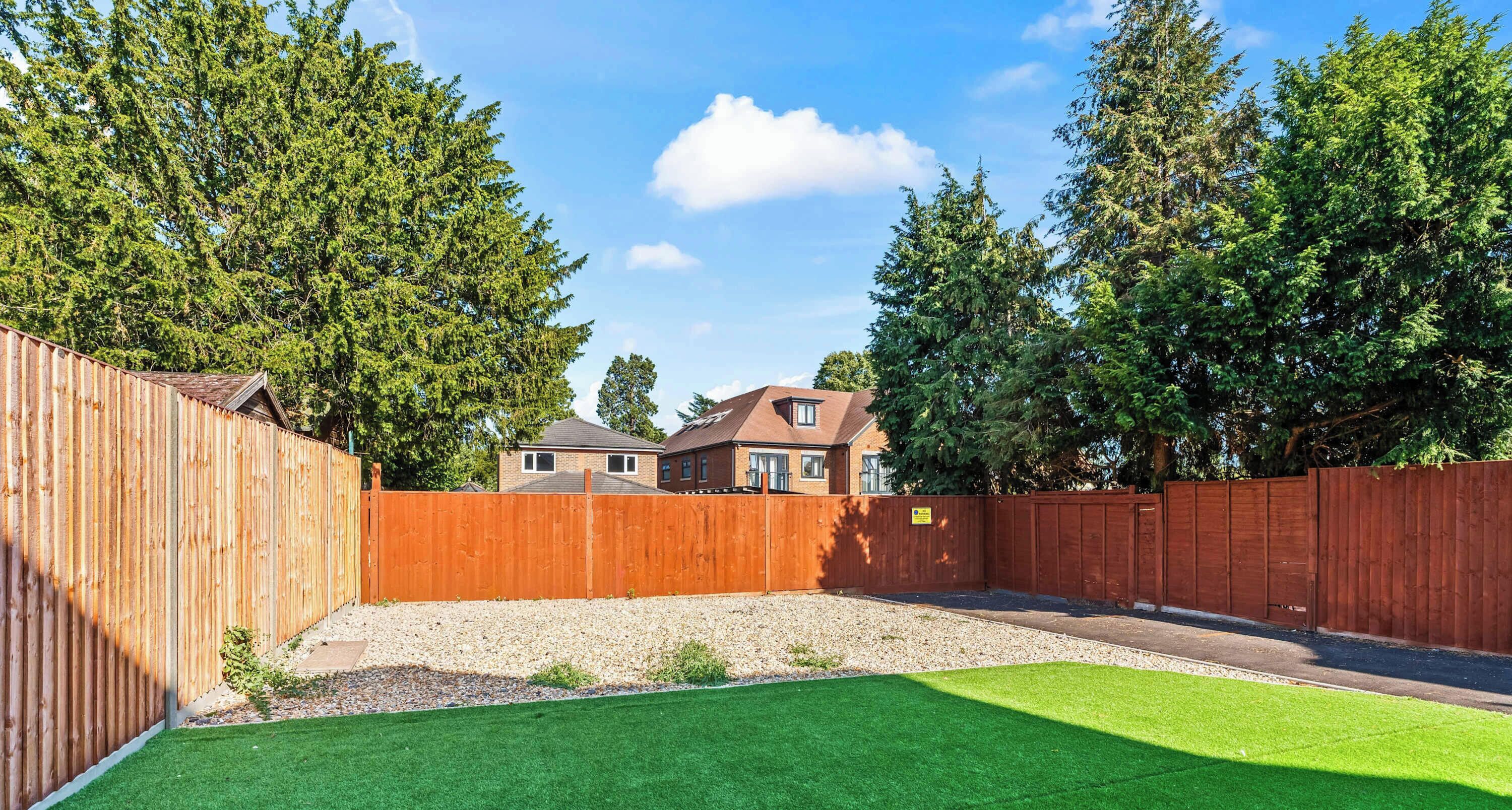 A fenced backyard with artificial grass, a wooden fence, and a house in the background.