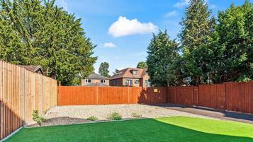 A fenced backyard with artificial grass, a wooden fence, and a house in the background.