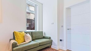 Una habitación con un sofá verde, una ventana y una puerta blanca.