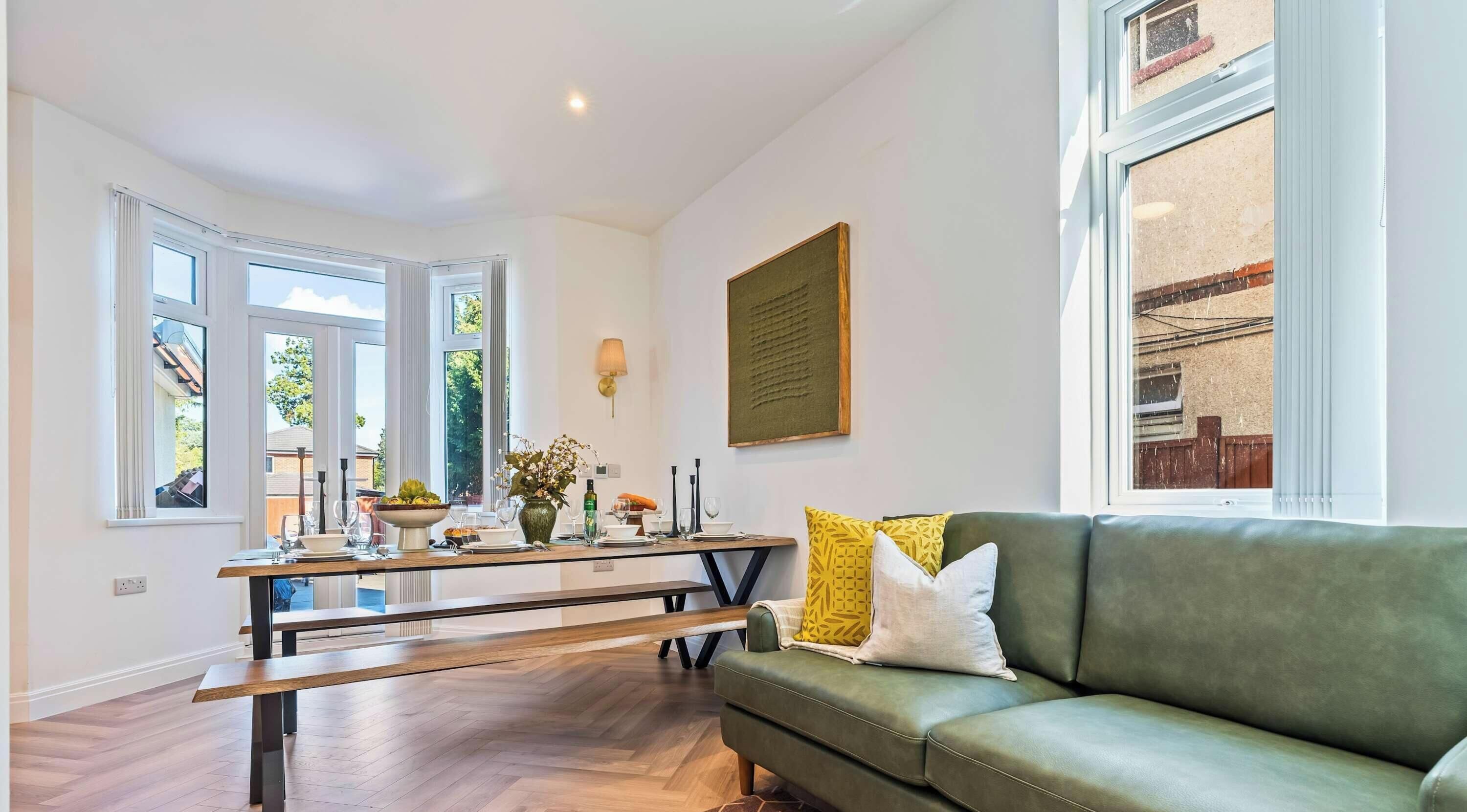 Un comedor con una mesa de madera, un sofá verde y una ventana con vista a un edificio.