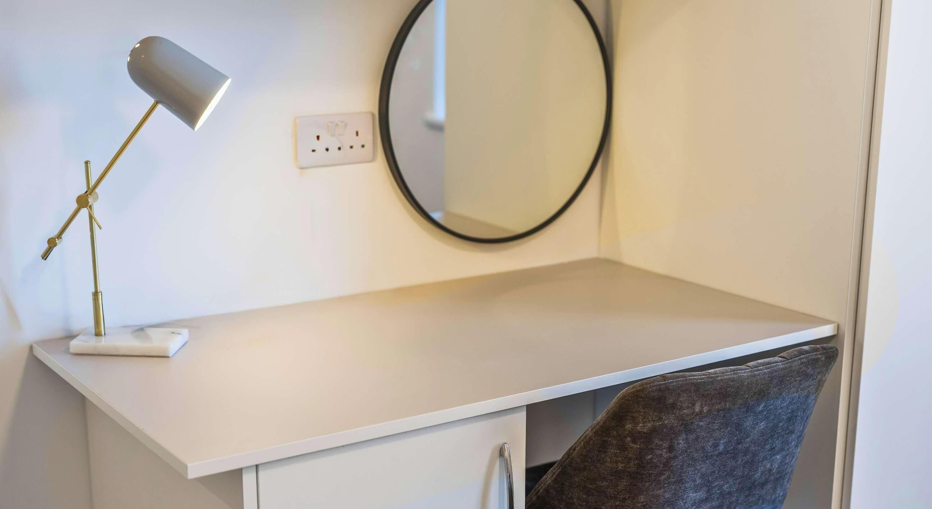 A white desk with a lamp, a mirror, and a chair in a room.