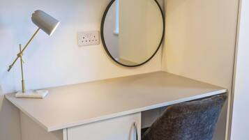 A white desk with a lamp, a mirror, and a chair in a room.