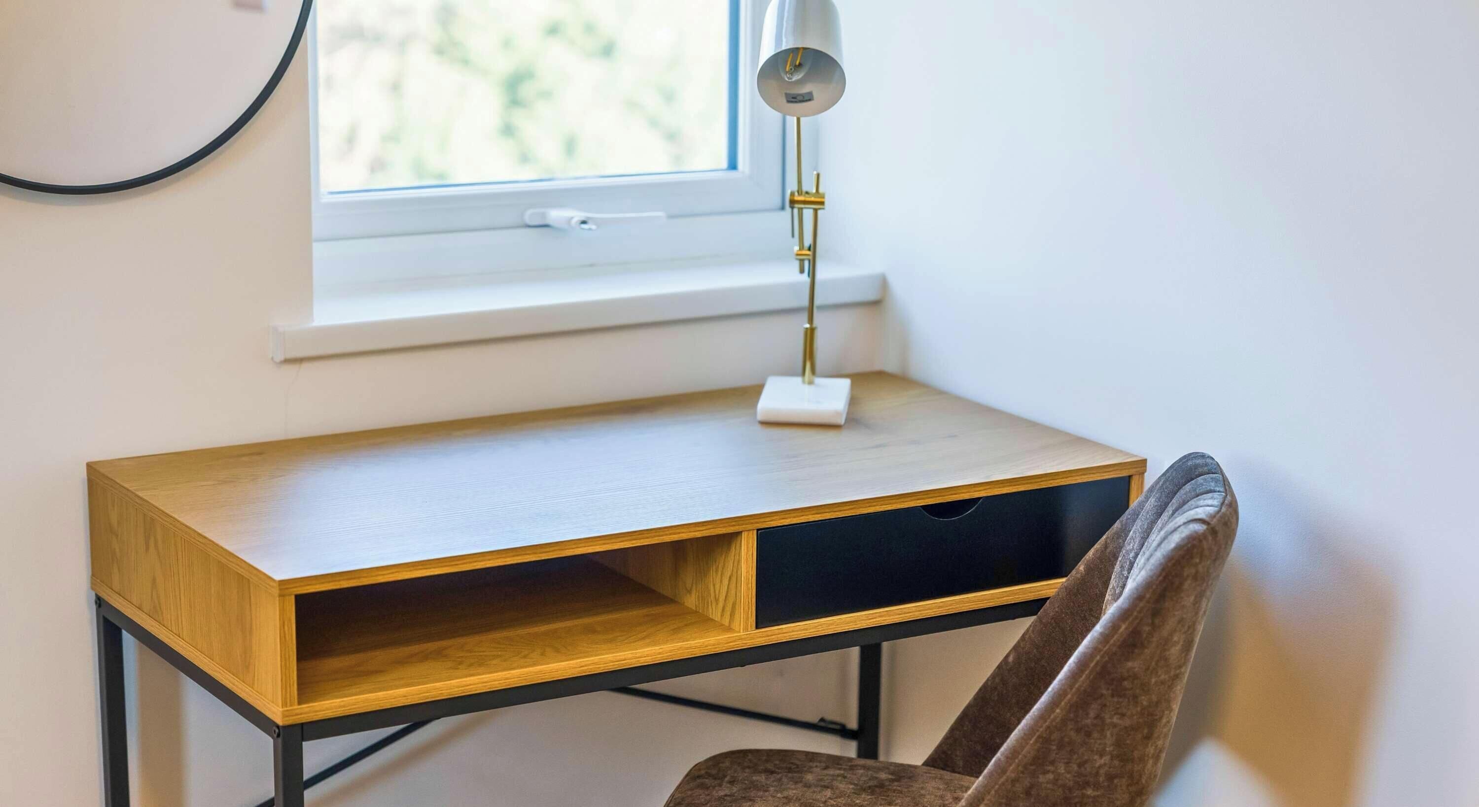 Escritorio de madera con una lámpara y una silla, cerca de una ventana.