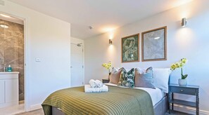 Ein modernes Schlafzimmer mit Bett, Nachttischen, einem Badezimmer und Kunstwerken an den Wänden.