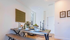 Un comedor con una mesa de madera dispuesta para cuatro, un banco y un florero con flores.