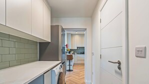 Una cocina moderna con armarios blancos, piso de espiga y lavadora a la vista.