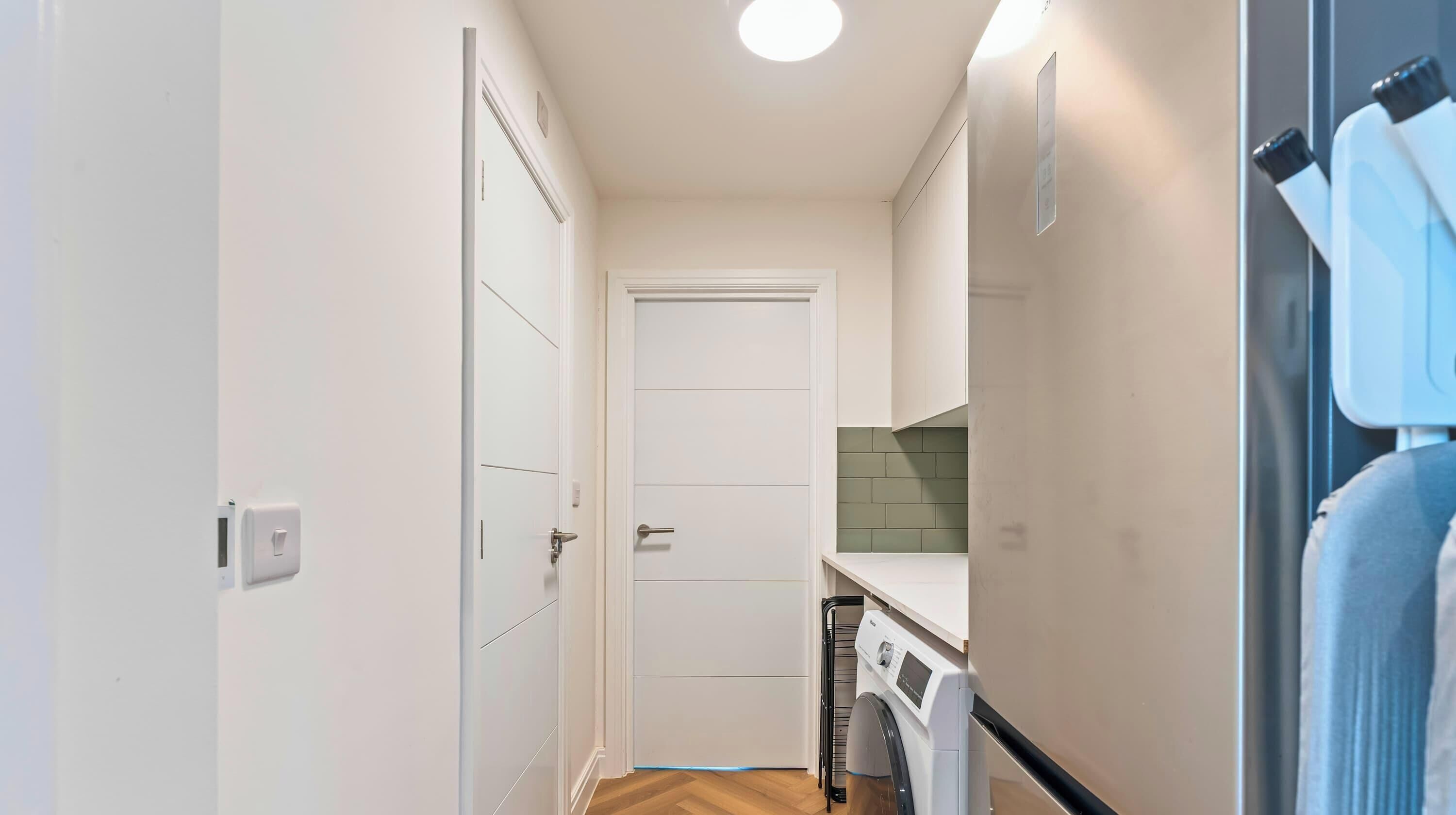 Un pasillo estrecho con una puerta al final, que da a un área de lavandería con lavadora y secadora.