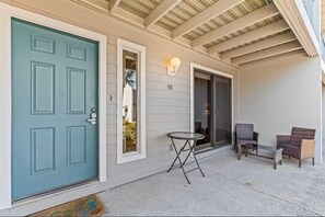 A house with a teal front door, a number '50' above the door, a small round table, and two wicker chairs outside. - Gulf Winds East #50 (Miramar Beach)