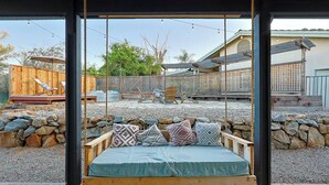 A swing bed with a view of a backyard with a wooden deck, chairs, and a stone wall. - 6BR SDSU - Pool & Spa - Poker/Game Rm - Sleep 20+ (San Diego)