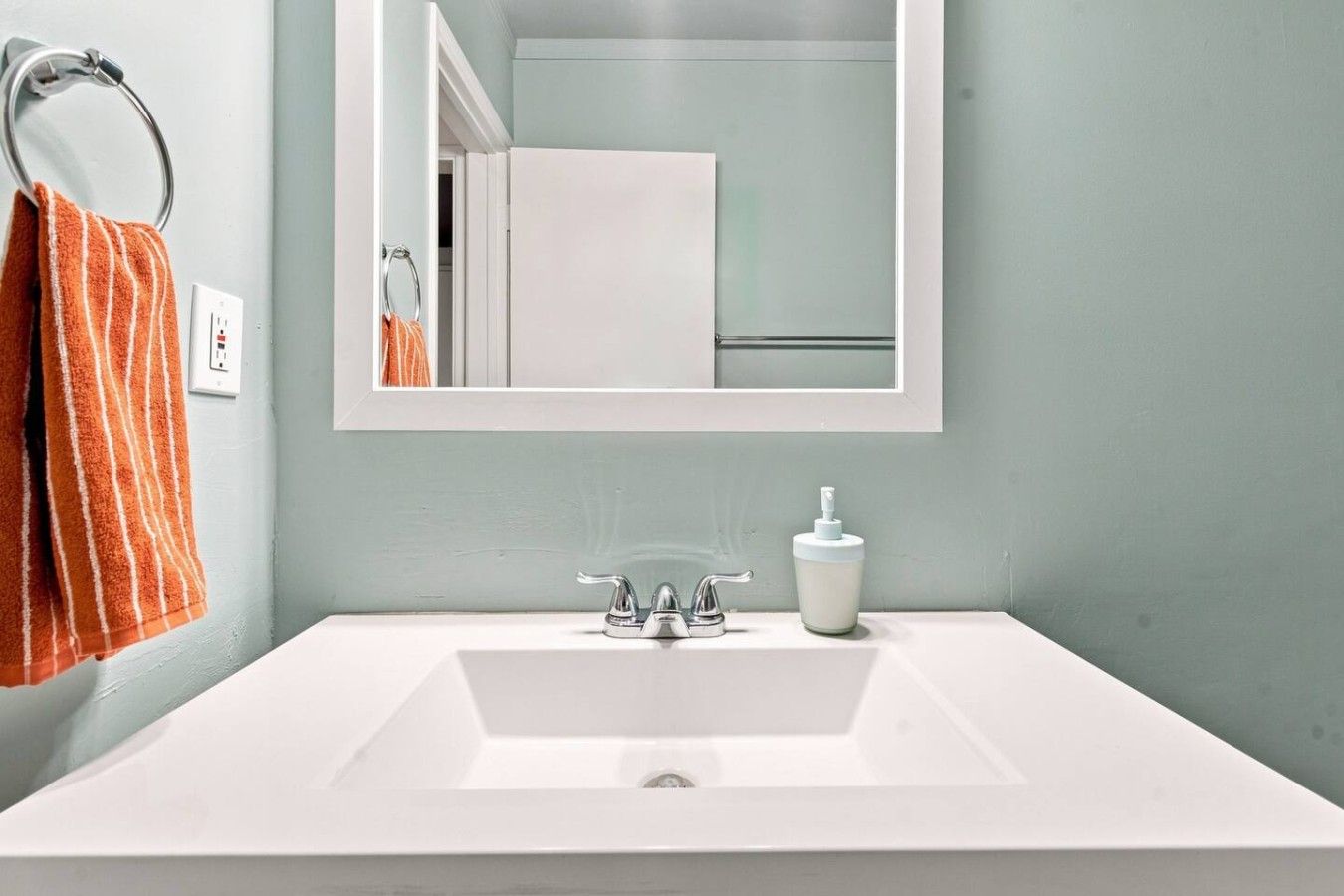 A bathroom with a white sink, a mirror, and an orange towel.