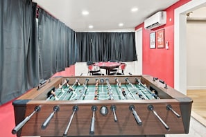 A room with a foosball table, a dining table, and a red wall with a framed picture. - SDSU Splash Royale 6BR - 12 Bed - Pool & Spa - Game Room - AC - Washer & Dryer (San Diego)