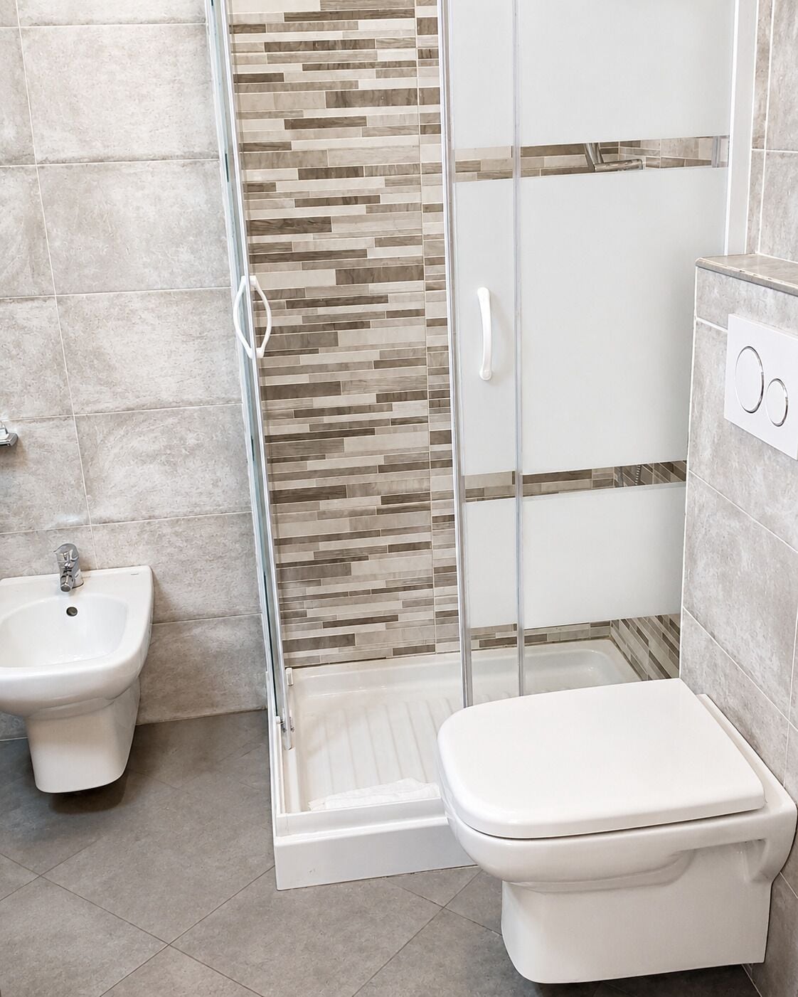 Un baño con bidé, inodoro y cabina de ducha de vidrio.