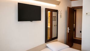A hotel room with a bed, a flat-screen TV mounted on the wall, a mirror, and a door leading to another room.
