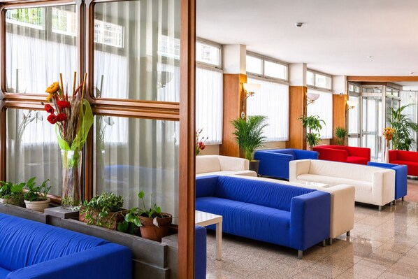 A hotel lobby with blue and red sofas, potted plants, and large windows.