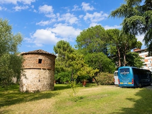 Una estructura de piedra, un autobús estacionado y árboles en un área cubierta de césped.
