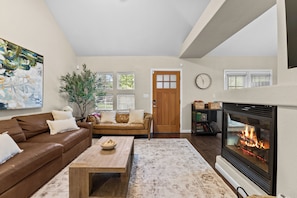 A living room with a fireplace, a brown leather sofa, a coffee table, and a painting on the wall. - New! Denver House Near Pearl St & Wash Park | Patio | Fire Pit | Fenced Yard (Denver)