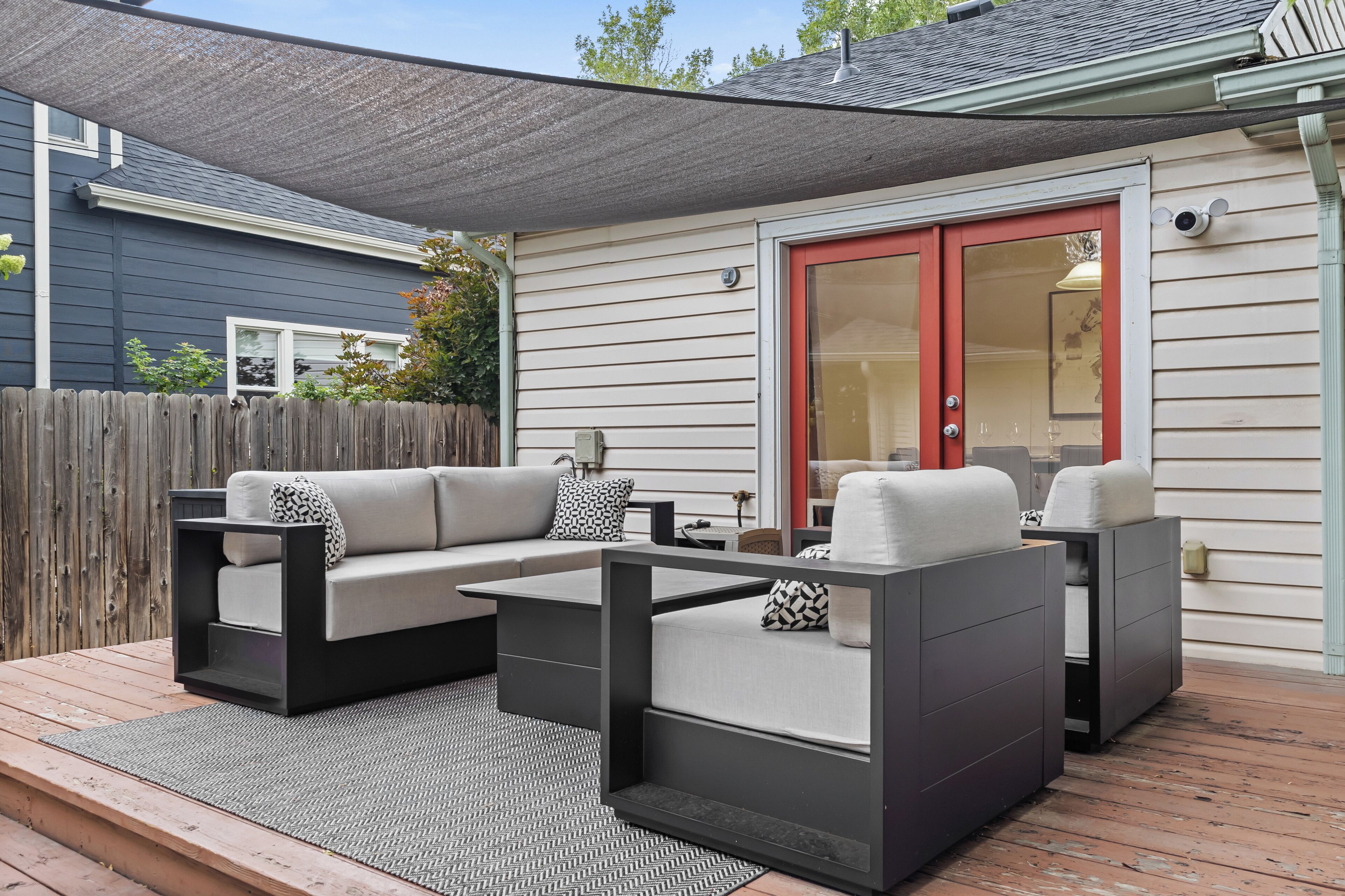 Eine Terrasse im Freien mit einem grauen Ecksofa, einem kleinen Tisch und einer roten Rutschtür.