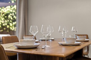 Una mesa de comedor dispuesta con platos, tazones y copas de vino, rodeada de sillas.