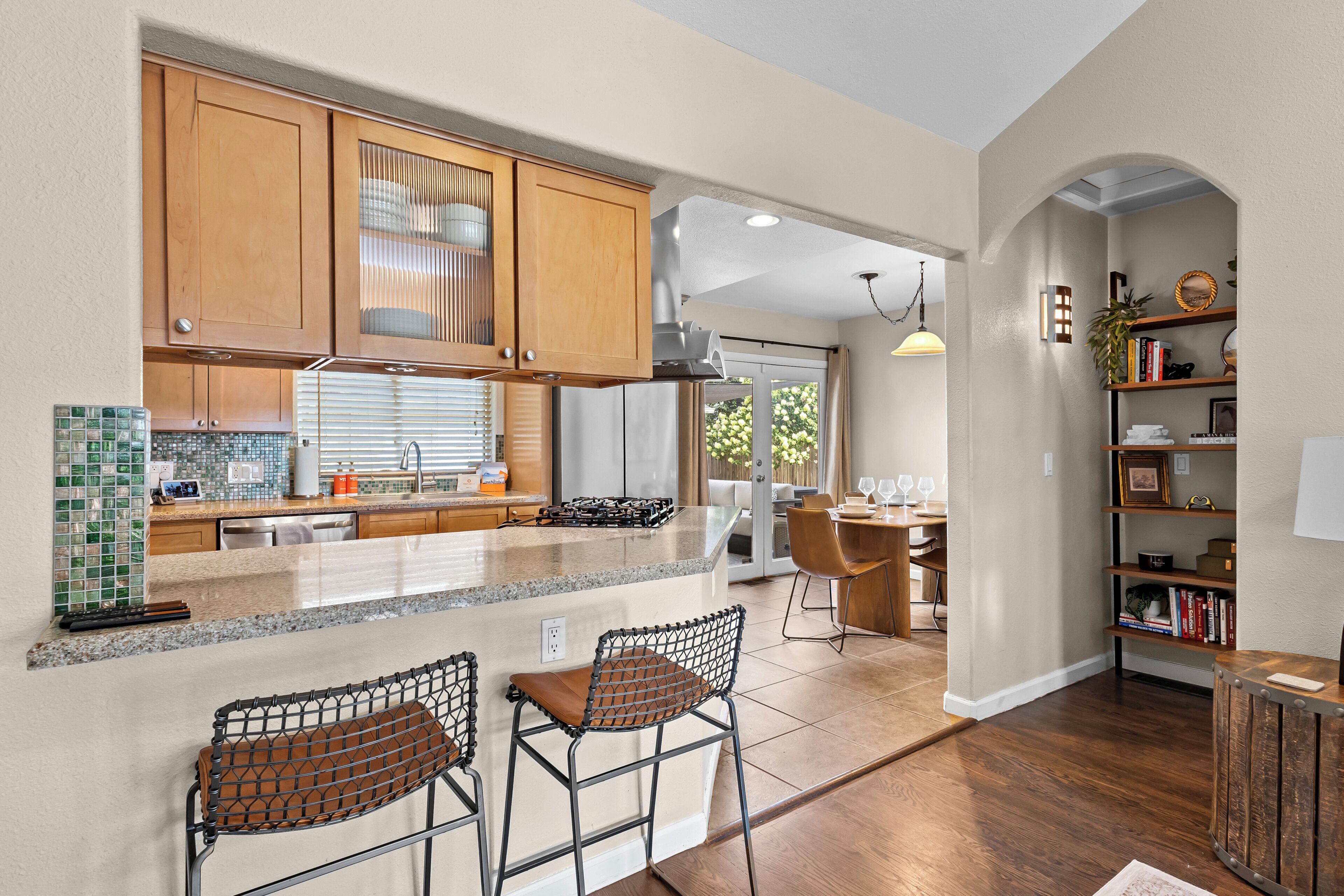 A modern kitchen with wooden cabinets, a stainless steel refrigerator, and a bar area with two stools.
