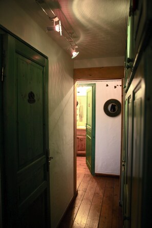 Un pasillo estrecho con suelo de madera, puertas verdes y un baño a la vista con un espejo.