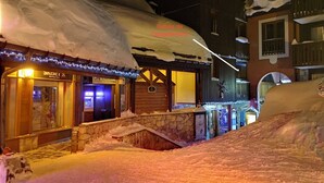 A snow-covered street with buildings, a stone wall, and a wooden structure with a sign. - Very comfortable apartment in Belle-Plagne, 50 m² (La Plagne Tarentaise)