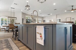 A modern kitchen with grey cabinets, a marble countertop, and a hanging towel with a Florida state map. - Lakefront 4-bedroom, 2.5-bath home on Lake Susan with a private dock and boat lift, a new 6-person hot tub, a paver deck with a built-in fire pit, and a Game Room with a pool table, darts and Golden Tee. Room for up to 10 guests. (Clermont)