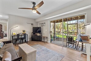Un salon spacieux doté d’un ventilateur de plafond, d’un téléviseur et d’une porte-fenêtre coulissante donnant sur une terrasse extérieure.