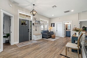 A spacious living area with a grey sofa, a wooden floor, and a large window providing natural light. - Lakefront 4-bedroom, 2.5-bath home on Lake Susan with a private dock and boat lift, a new 6-person hot tub, a paver deck with a built-in fire pit, and a Game Room with a pool table, darts and Golden Tee. Room for up to 10 guests. (Clermont)