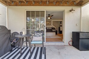 Un espace extérieur aménagé en terrasse, avec une table et des chaises, un barbecue et une porte-fenêtre coulissante donnant sur un espace de vie intérieur.