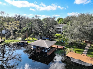 A lakeside property with a dock, a covered boat house, and a house with a solar panel roof. - Waterfront 4BR/2.5BA home with direct access to the Clermont Chain of Lakes! Private dock with boat slips & 1 motorized lift — perfect for boating & kayaking.  Gourmet kitchen, luxurious primary suite, available kayaks onsite. (Clermont)