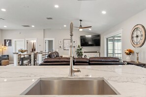 A modern kitchen with a stainless steel sink, marble countertop, and a ceiling fan. - Lakefront 4-bedroom, 2.5-bath home on Lake Susan with a private dock and boat lift, a new 6-person hot tub, a paver deck with a built-in fire pit, and a Game Room with a pool table, darts and Golden Tee. Room for up to 10 guests. (Clermont)
