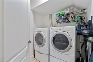 A laundry room with two stacked front-loading washing machines, a drying rack with various items, and a vacuum cleaner. - Waterfront 4BR/2.5BA home with direct access to the Clermont Chain of Lakes! Private dock with boat slips & 1 motorized lift — perfect for boating & kayaking.  Gourmet kitchen, luxurious primary suite, available kayaks onsite. (Clermont)