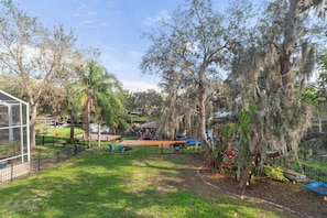A fenced outdoor area with a wooden deck, a glass structure, and trees with hanging moss. - Waterfront 4BR/2.5BA home with direct access to the Clermont Chain of Lakes! Private dock with boat slips & 1 motorized lift — perfect for boating & kayaking.  Gourmet kitchen, luxurious primary suite, available kayaks onsite. (Clermont)