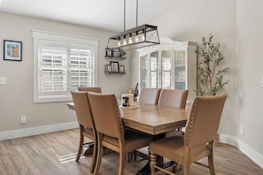 A dining room with a wooden table and chairs, a hanging light fixture, and a window with blinds. - Waterfront 4BR/2.5BA home with direct access to the Clermont Chain of Lakes! Private dock with boat slips & 1 motorized lift — perfect for boating & kayaking.  Gourmet kitchen, luxurious primary suite, available kayaks onsite. (Clermont)