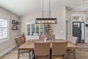 A dining room with a wooden table, beige upholstered chairs, a decorative light fixture, and a white cabinet with glass doors. - Waterfront 4BR/2.5BA home with direct access to the Clermont Chain of Lakes! Private dock with boat slips & 1 motorized lift — perfect for boating & kayaking.  Gourmet kitchen, luxurious primary suite, available kayaks onsite. (Clermont)