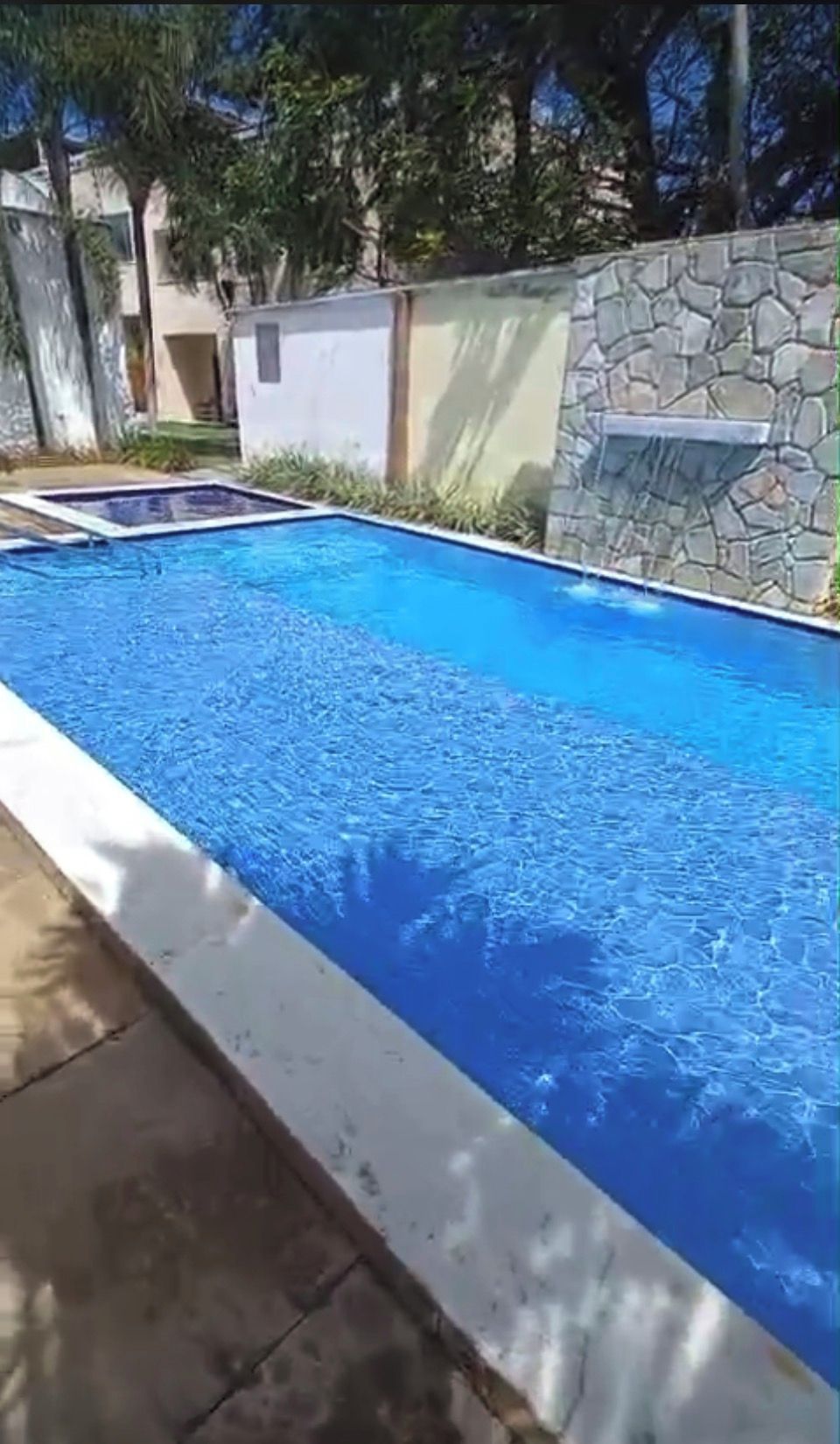 Une piscine rectangulaire avec un mur en pierre d’un côté et un bord en béton.