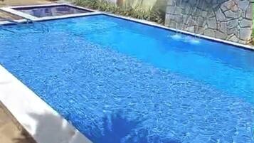 Une piscine rectangulaire avec un mur en pierre d’un côté et un bord en béton.