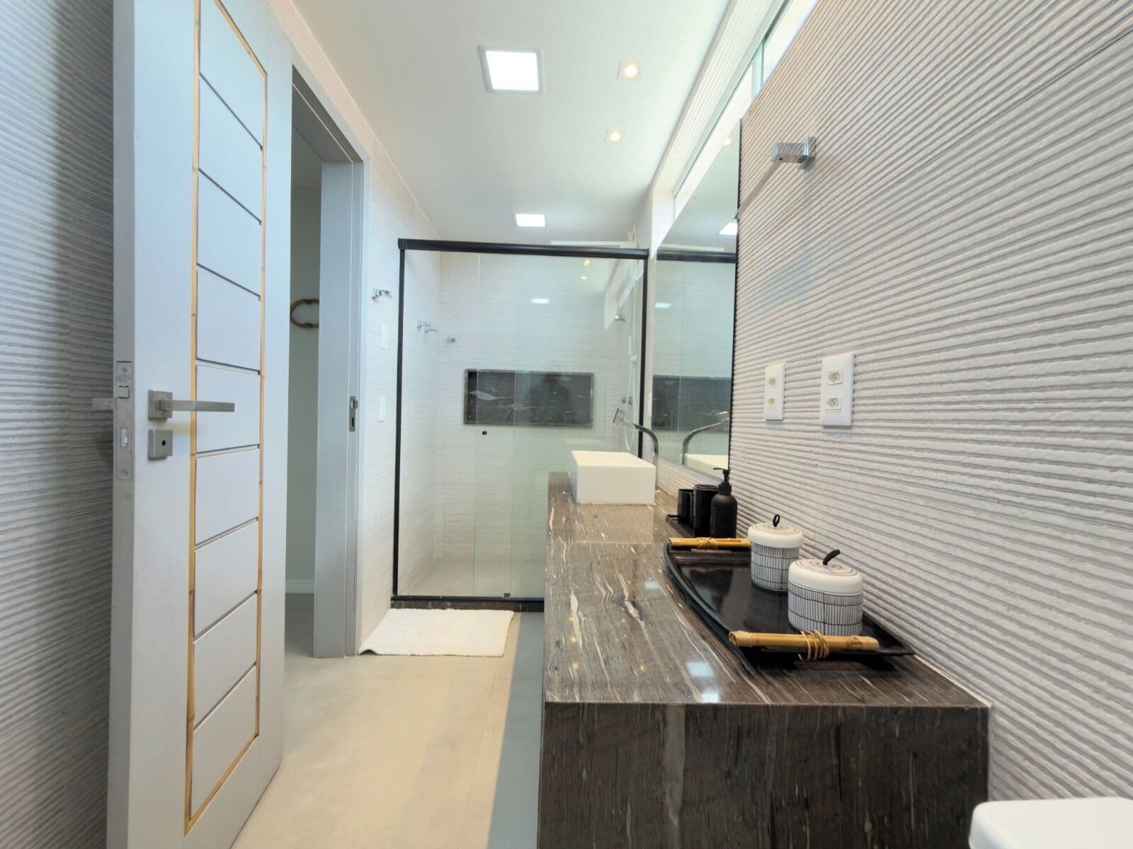 Une salle de bain moderne avec une douche à parois de verre, un lavabo en marbre foncé et un grand miroir.