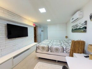Una camera da letto con un letto, una TV a schermo piatto montata su una parete di mattoni bianchi, una ventola a soffitto e un condizionatore d'aria.