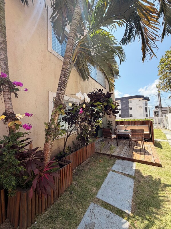 A patio with a wooden deck, outdoor furniture, and a variety of plants including orchids and a palm tree.