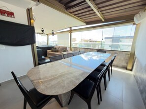 A modern dining area with a long table and chairs, a sofa, and a view of the city through large windows.